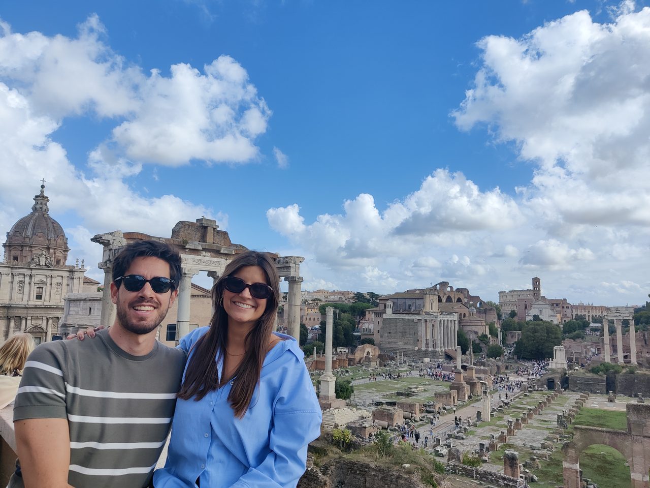 Joana and João smiling above the Roman Forum on a bright day.